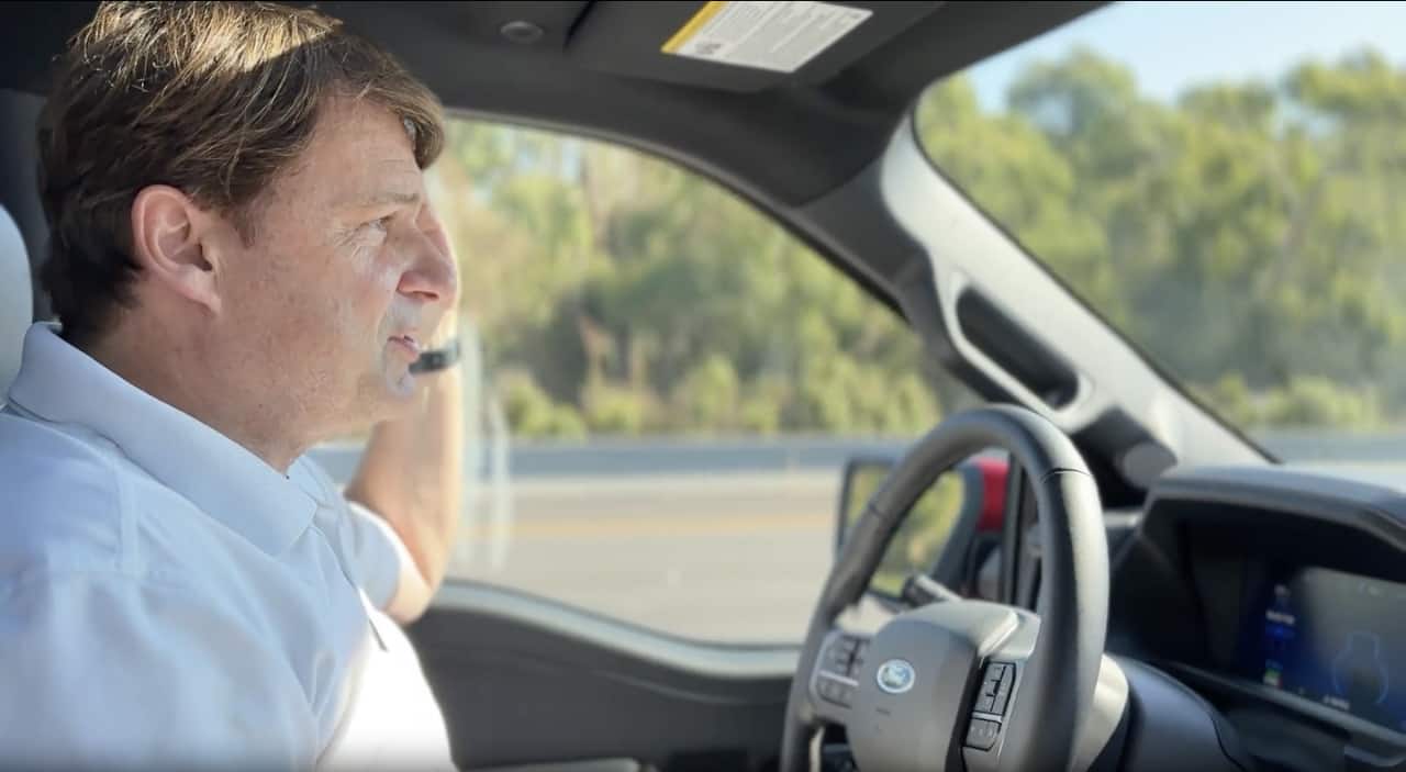 Viewed from the passenger seat, a man drives a vehicle with no hands on the wheel, displaying hands-free driving capabilities of the vehicle.